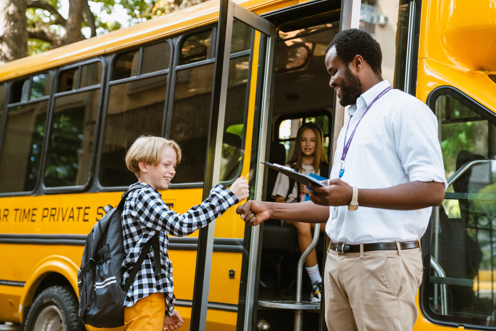 A Teacher Taking Attendance of Students Getting on the Bus